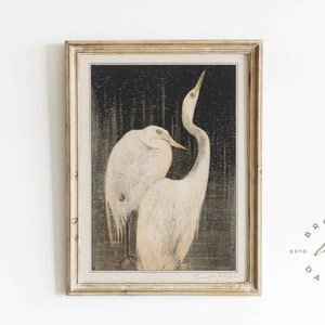 May include: A framed print of two white egrets standing in a dark, textured background. The egrets are facing each other, with their necks curved and their heads tilted. The print is in a light wood frame.