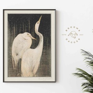 May include: A black and white print of two white egrets standing in a dark forest. The print is framed in a black frame and has the artist's signature in the bottom right corner.