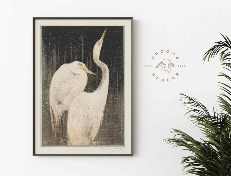 May include: A black and white print of two white egrets standing in a dark forest. The print is framed in a black frame and has the artist's signature in the bottom right corner.