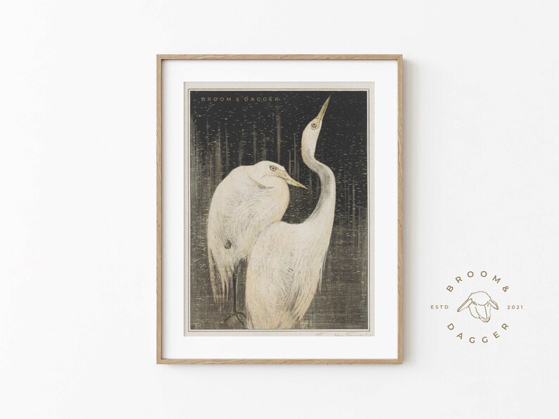 May include: A framed print of two white egrets standing in a dark, textured background. The print is titled "Broom & Dagger" and features a stylized illustration of the birds.