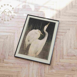 May include: A framed print of a black and white illustration of two white herons standing in a dark, watery environment. The herons are facing each other, with their necks curved and their beaks touching. The print is set against a light wood background.