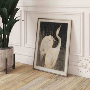 May include: A framed print of a black and white illustration of two white herons with long necks and beaks. The herons are standing in a forest setting with a dark background. The print is framed in a silver frame.