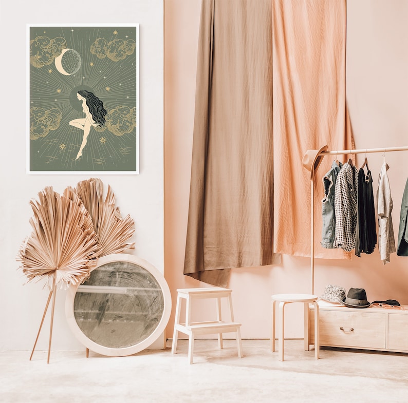 May include: A framed print of a woman sitting on a cloud with a crescent moon and stars in the background. The print is in a white frame and is hanging on a white wall.