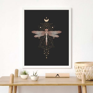 May include: A framed print with a black background featuring a pink dragonfly with gold geometric shapes and a crescent moon.