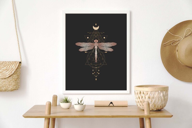 May include: A framed print with a black background featuring a pink dragonfly with gold geometric shapes and a crescent moon.