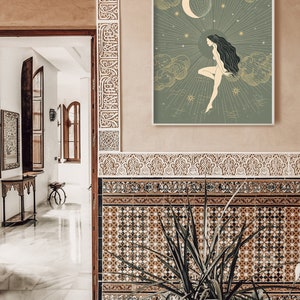May include: A green and gold illustration of a woman standing on a cloud with a crescent moon and stars in the background. The illustration is framed and hanging on a wall with brown and white patterned tiles.