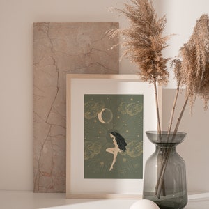 May include: A framed print with a green background featuring a woman with long dark hair sitting on a cloud with a crescent moon and stars in the background.