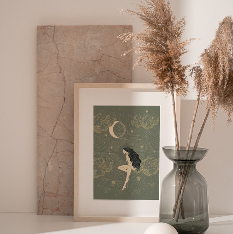 May include: A framed print with a green background featuring a woman with long dark hair sitting on a cloud with a crescent moon and stars in the background.