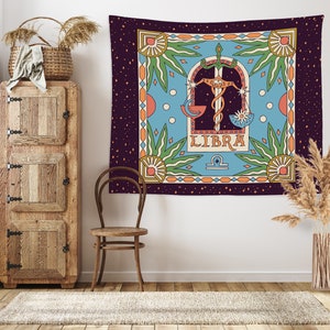 May include: A tapestry featuring a Libra zodiac sign with a scale, sword, and stars on a blue background. The tapestry has a colorful border with a purple background and a repeating pattern of stars.