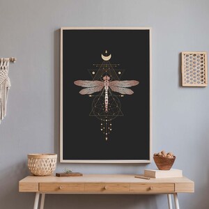 May include: A black and gold geometric print featuring a dragonfly with a crescent moon and stars. The dragonfly is pink and gold with a black outline.