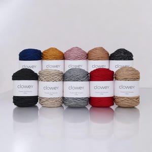 Può includere: Una collezione di dieci rocchetti di filato in vari colori, tra cui blu navy, oro, rosa, marrone, nero, beige, grigio, rosso e marrone chiaro. Ogni rocchetto ha un'etichetta bianca con il marchio "clowex". Il filato è disposto su due file.