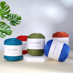 May include: An assortment of colorful macrame yarn balls in teal, red, olive green, and blue. Each ball is labeled with the brand name "clowex" and "Polyester Soft Macrame PLUS". The yarn is displayed on a white surface with a monstera leaf in the background.
