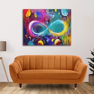 May include: Abstract painting of an infinity symbol in vibrant colors, including blue, yellow, pink, and purple, on a dark background. The painting is framed and hanging on a wall above a brown sofa.