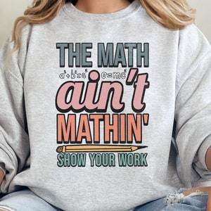 May include: A gray sweatshirt with the text "The Math ain't Mathin' Show Your Work" in colorful letters. The text is stylized with a pencil graphic.