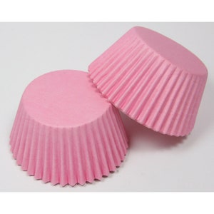 May include: Two pink cupcake cases, made of paper, with a fluted design. The cases are folded and stacked on top of each other.