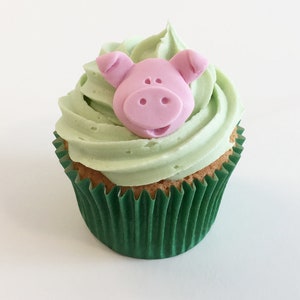 Può includere: Un cupcake verde con glassa verde chiaro e un topper a forma di maiale rosa.