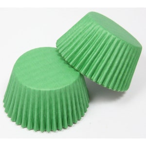 May include: Two green cupcake cases, made of paper, with a fluted edge.