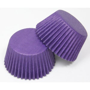 May include: Two purple cupcake cases, with a fluted design. The cases are made of paper and are designed to be used in a muffin tin.