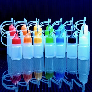 May include: A collection of 14 clear plastic bottles with droppers, each filled with a different coloured liquid. The bottles are arranged in a row on a blue surface.