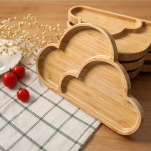 Op de afbeelding: Een set van vier houten, wolkvormige borden. De borden zijn gemaakt van natuurlijk bamboe en hebben een lichtbruine kleur. De borden zijn op elkaar gestapeld, met het bovenste bord als het grootste.