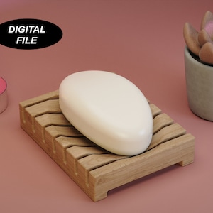 Pode incluir: Um modelo 3D imprimível de um saboneteira com uma barra de sabão. A saboneteira é feita de madeira e tem um design ondulado. O sabão é branco e de forma oval. A imagem também inclui uma pequena vela rosa e uma suculenta em vaso.