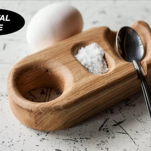 May include: A wooden egg holder with a salt well and a spoon rest. The holder is made of light brown wood and has a natural finish. The salt well is filled with white salt. The spoon rest is empty. The holder is sitting on a white surface. DIGITAL FILE STL
