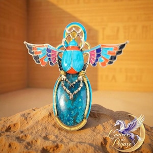 Peut inclure: Un pendentif scarabée turquoise et doré avec des ailes colorées. Le pendentif présente une grande pierre turquoise et un travail de métal complexe. Les ailes sont ornées d'émail noir, orange, rose et bleu. Le pendentif est exposé sur une surface sablonneuse.
