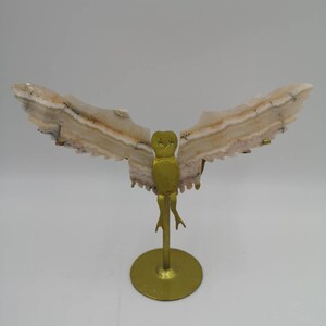 Peut inclure: Une sculpture de hibou blanche et brune avec des ailes en métal doré et un socle. Le hibou est fait de pierre naturelle et présente un design détaillé.
