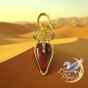 Peut inclure: Un pendentif doré avec une pierre rouge-brun en forme de goutte d'eau. Le pendentif présente un design orné avec une figure ailée en haut. L'arrière-plan montre un paysage désertique avec des dunes de sable. Il s'agit probablement d'un bijou.