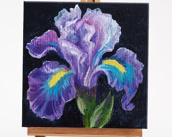 May include: A small painting of a purple iris flower on a black background. The painting is on a small easel.