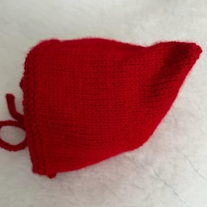 May include: A red knitted baby bonnet with a tie string.