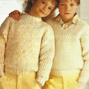 May include: Two children wearing cream coloured knit sweaters. The girl is wearing a high neck sweater and the boy is wearing a v-neck sweater.