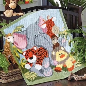 Può includere: Una coperta per neonati all'uncinetto fatta a mano con un tema di animali della giungla. La coperta presenta un elefante, una tigre, un leone e una giraffa in colori vivaci. La coperta è esposta su una culla di legno scuro.