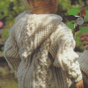 May include: A white knitted hooded sweater with a cable knit pattern. The sweater is being worn by a child.
