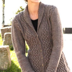 Puede incluir: Un cárdigan marrón tejido por cable con cuello chal y cierre de botones. El suéter presenta intrincados patrones tejidos en la parte delantera y las mangas. El cárdigan es de peso medio y parece estar hecho de lana o una mezcla de lana.