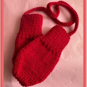May include: Red knitted mittens with a matching red knitted strap. The mittens are made with a simple knit stitch and have a textured appearance.