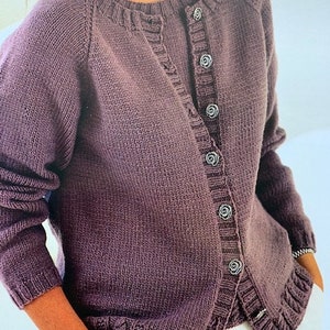 Może przedstawiać: Fioletowy kardigan z dzianiny z zapięciem na guziki i ściągaczem na dole. Kardigan ma okrągły dekolt i długie rękawy.