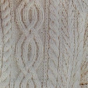 May include: Close-up of a cream-coloured knitted jumper with a cable knit pattern.