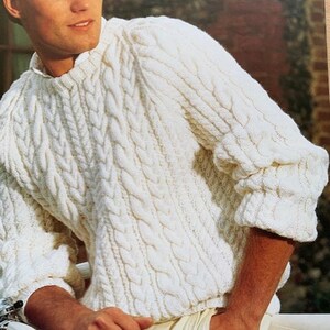 May include: Cream-colored cable knit sweater with a crew neck and long sleeves. The sweater features a textured, woven design. The sleeves have a ribbed cuff. The model is wearing cream-colored pants.