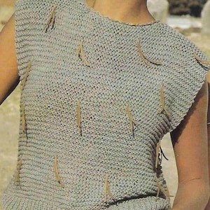 Puede incluir: Un top de punto sin mangas con un degradado de color verde claro y gris. El top tiene un escote redondo y está decorado con detalles de flecos de cuero marrón.