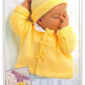 May include: A yellow knitted baby cardigan with a bow detail on the front. The cardigan is worn by a sleeping baby wearing a yellow knitted hat.