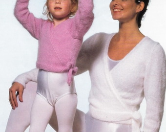 May include: A woman and a young girl wearing white and pink knit wrap sweaters. The woman is wearing a white leotard and the girl is wearing a white leotard and white tights.