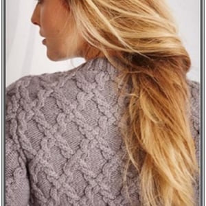 Könnte beinhalten: Nahaufnahme eines grauen Zopfstrickpullovers. Der Pullover hat ein strukturiertes, gewebtes Muster. Die Person hat lange, blonde Haare.