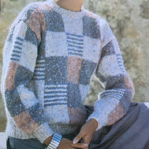May include: A light blue, grey, and pink checkered sweater with a round neckline. The sweater is made of a soft, fuzzy yarn.