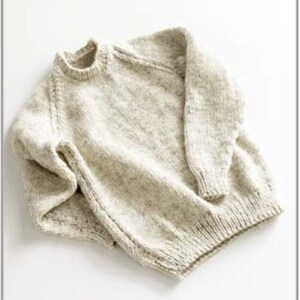 Puede incluir: Un suéter beige claro de cuello redondo con mangas largas. El tejido de punto tiene una apariencia texturizada y puños y dobladillo acanalados. El suéter está doblado sobre una superficie blanca.