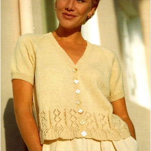 Puede incluir: Un cárdigan de punto de color crema con mangas cortas y cuello en V. El cárdigan tiene un cierre de botones con botones nacarados y un delicado ribete de encaje en la parte inferior.