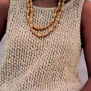 Puede incluir: Un top sin mangas de color beige claro con un diseño de tejido abierto. El top tiene un cuello redondo y una apariencia de ganchillo texturizado. Se lleva un collar de cuentas de madera de doble hebra.