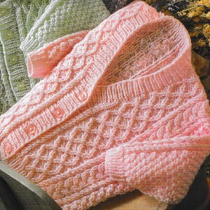 May include: A pink knitted cardigan with a cable knit pattern and button closures.