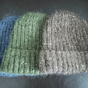 Puede incluir: Tres gorros de punto de diferentes colores: azul, verde y marrón. Los gorros están hechos de un hilo suave y texturizado.