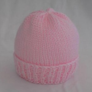 May include: A soft pink knitted baby hat. The hat features a ribbed brim and a rounded crown. The knit is a fine gauge, creating a smooth texture. This handmade hat is designed for infants and toddlers.